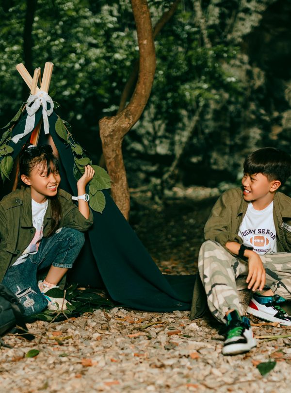 Two kids in a forest campground having fun with a tent and campfire.